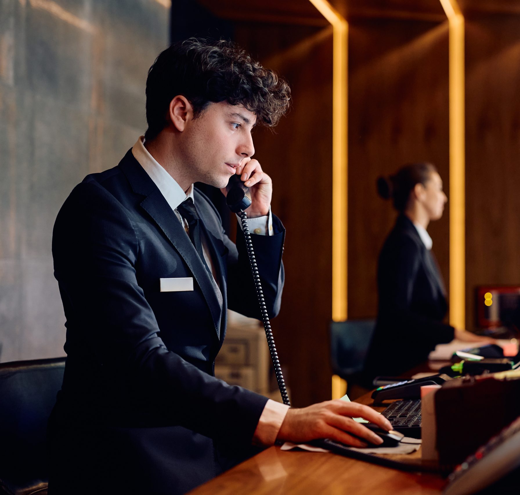 Hotel manager using computer while talking on the phone at reception desk.